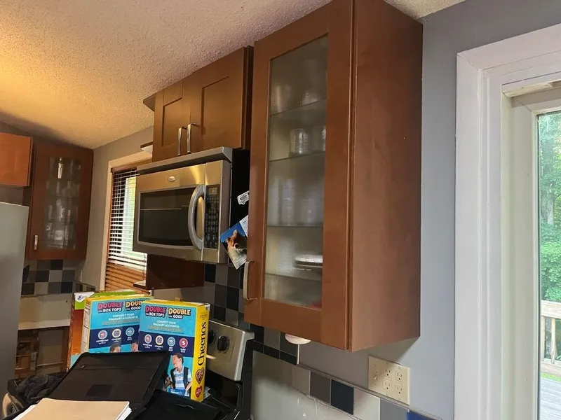 Kitchen cabinets above a microwave with cereal boxes and a laptop on the counter below.