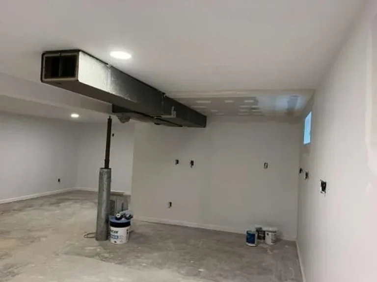 Unfinished basement with exposed ductwork, concrete floor, and paint supplies on the floor.