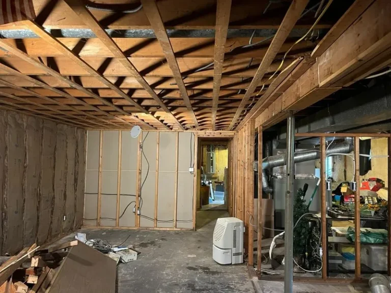 Unfinished basement with exposed wooden beams, insulation, and scattered construction materials.
