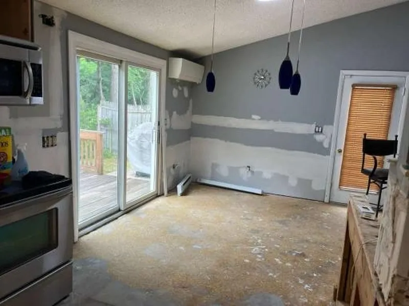Empty kitchen with unfinished walls, bare floor, sliding glass door, and hanging pendant lights.