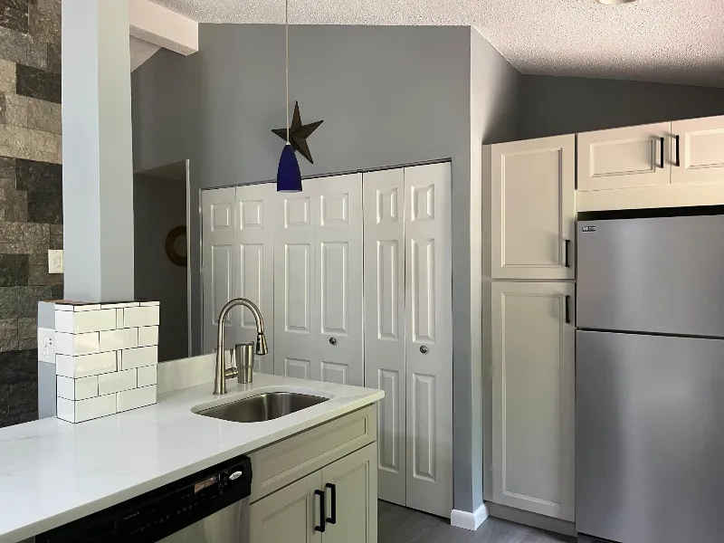 Modern kitchen corner with white cabinets, stainless steel refrigerator, and sink on a white countertop.